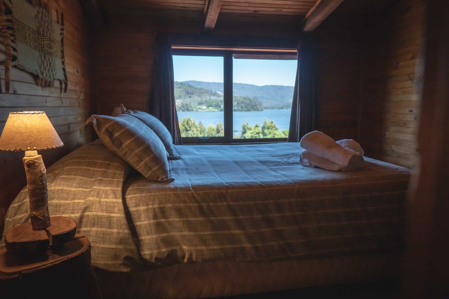Dormitorio de madera con cama matrimonial y ventana con vista al lago Lanalhue